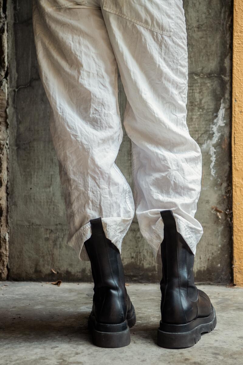 A man's legs, seen from behind, in white pants and black boots.