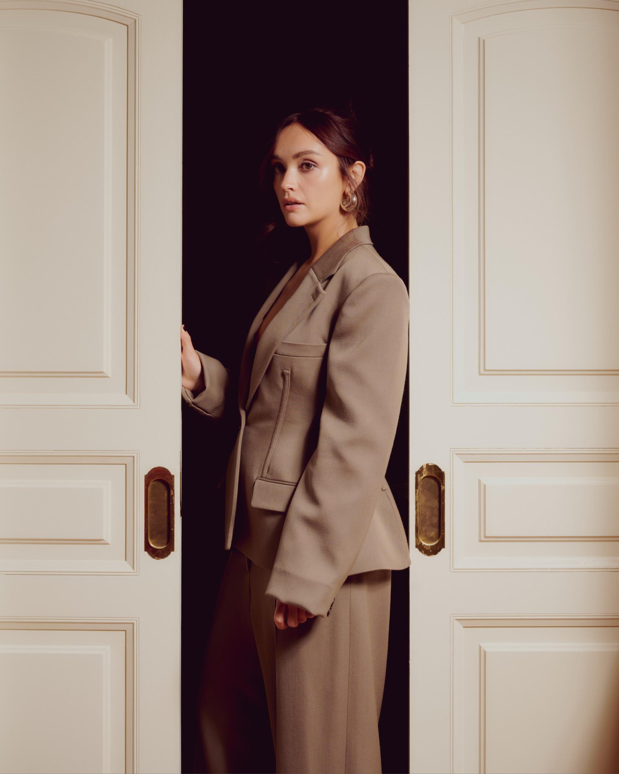 Olivia Cooke standing between two white doors.