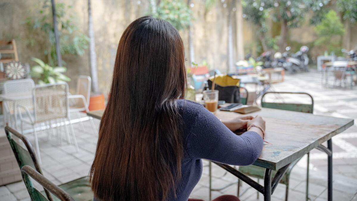 A girl sits at a cafe table with her back to the camera.