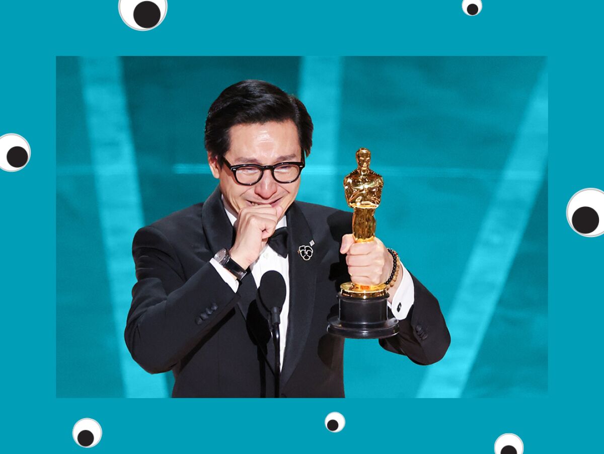 An Asian man in a tux and glasses emotionally holds up an Oscar.