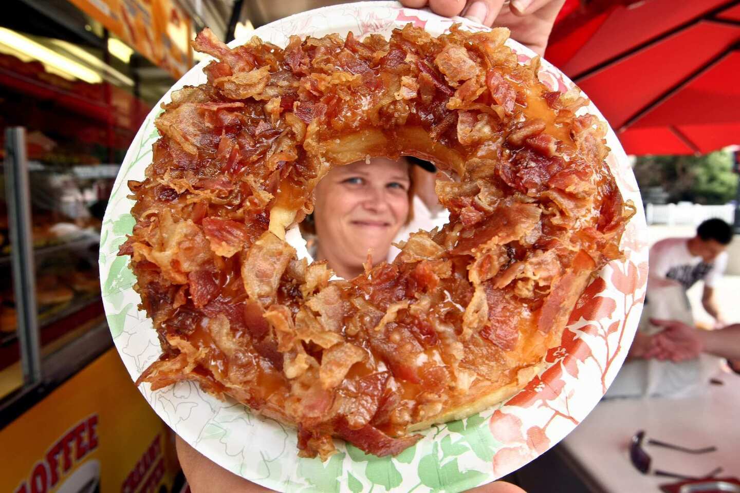 Barbie Holley displays a maple bacon doughnut on the menu at the Texas Donuts stand at the Los Angeles County Fair in Pomona. The maple bacon doughnut consists of a Big D glazed doughnut, warm maple icing and hickory smoked bacon.