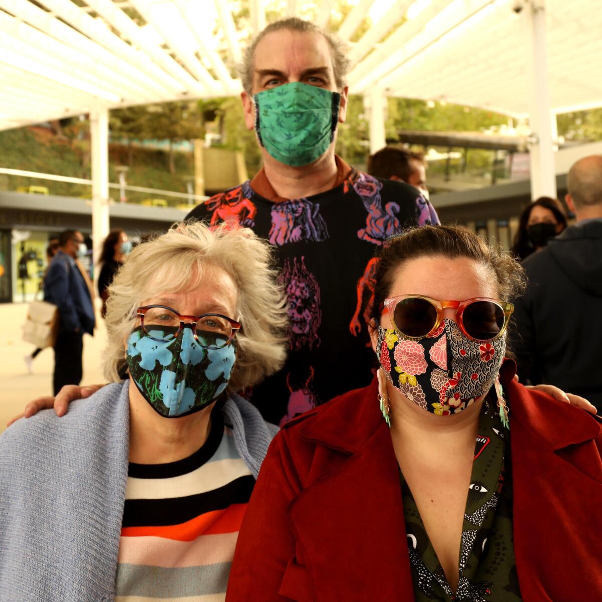 A man and two women in colorful face masks pose for a photo.