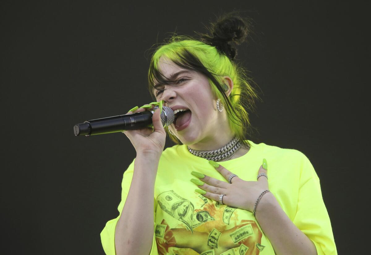 Billie Eilish, with florescent green hair and nails, sings into a microphone.