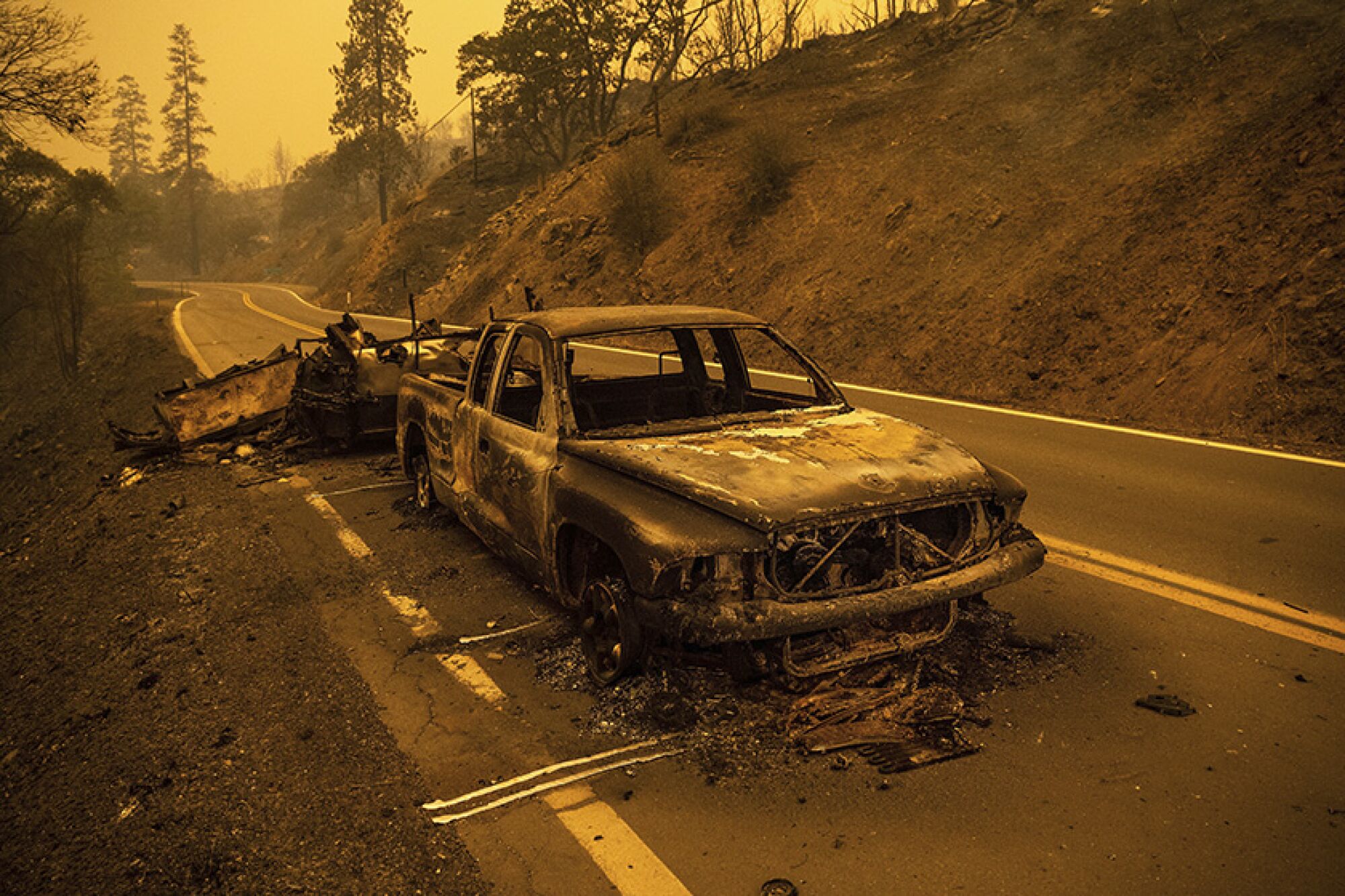 A charred truck sits on a smoky highway