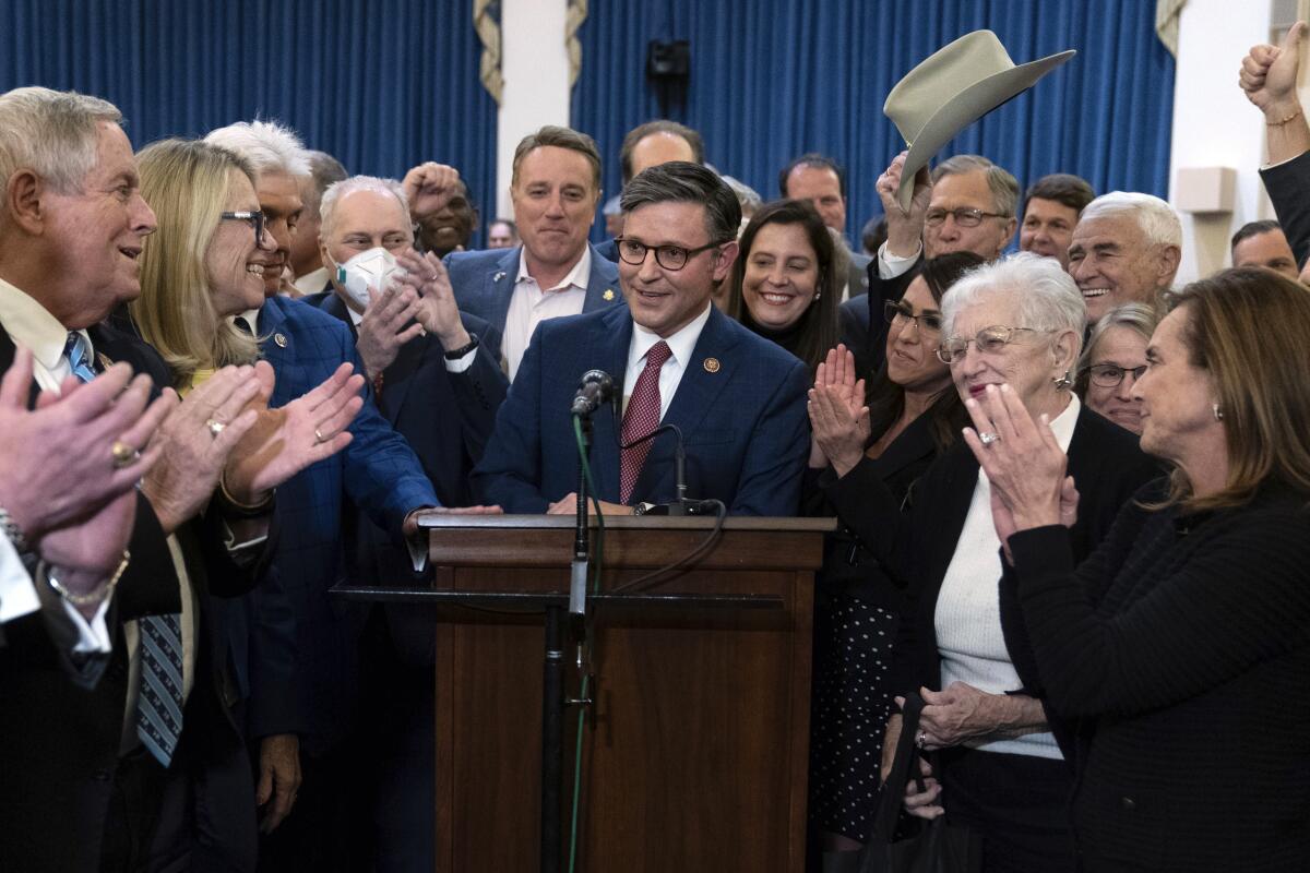 A man speaks at a podium while people surrounding him clap their hands
