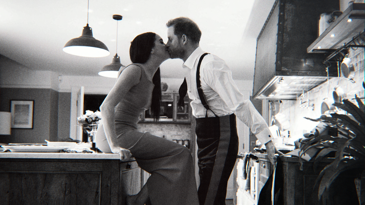 A woman with long dark hair sits on a kitchen counter kissing a man