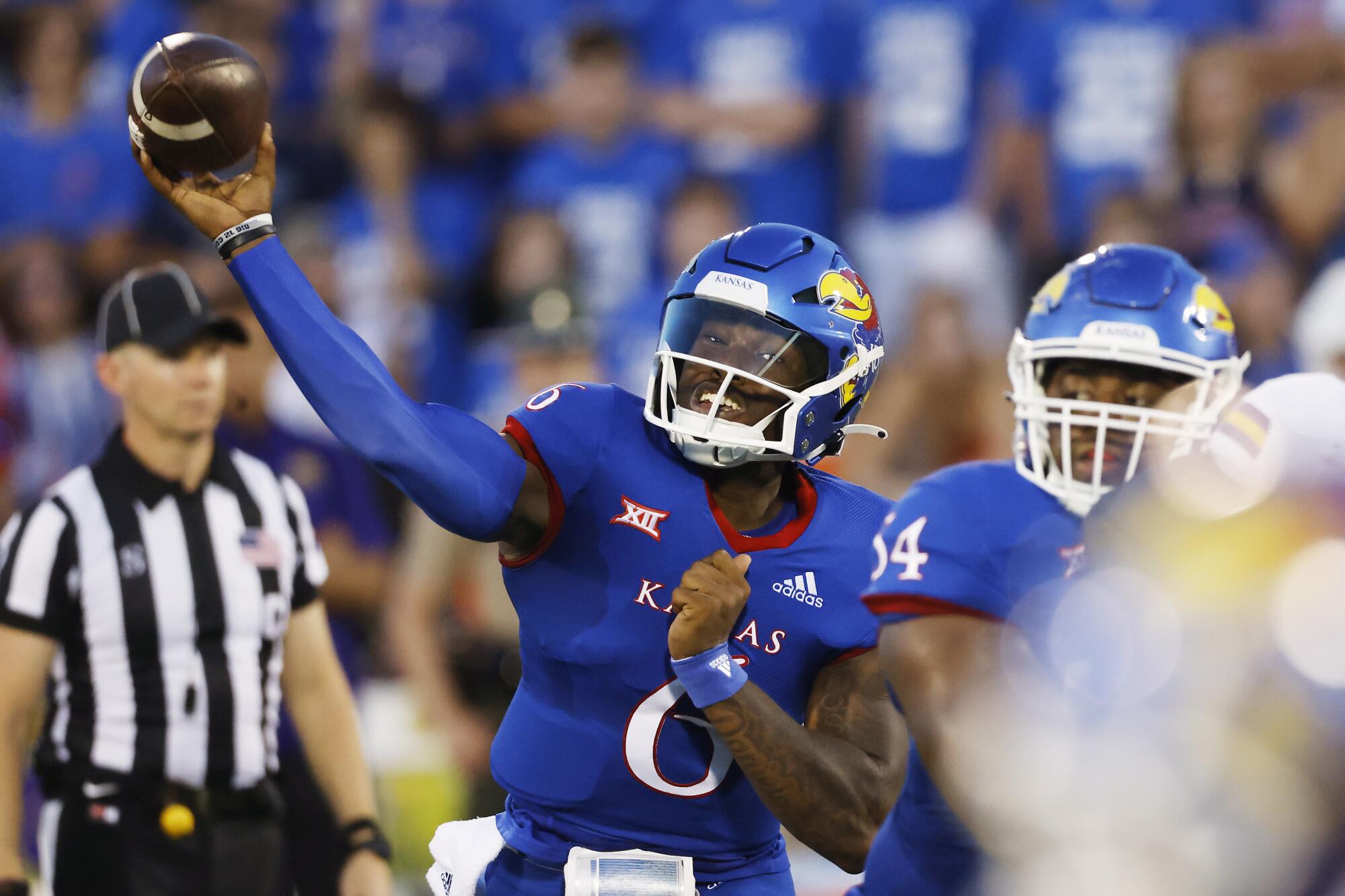 Kansas quarterback Jalon Daniels passes a football in front of a referee and teammate during a game.