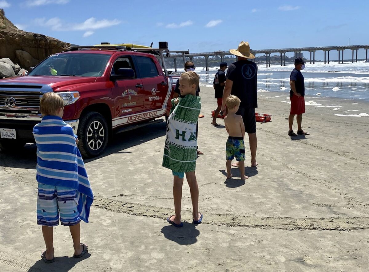 Neil Garrett and his children talk to San Diego lifeguards after Garrett helped rescue a young girl from the waves north of Scripps Memorial Pier at La Jolla Shores.