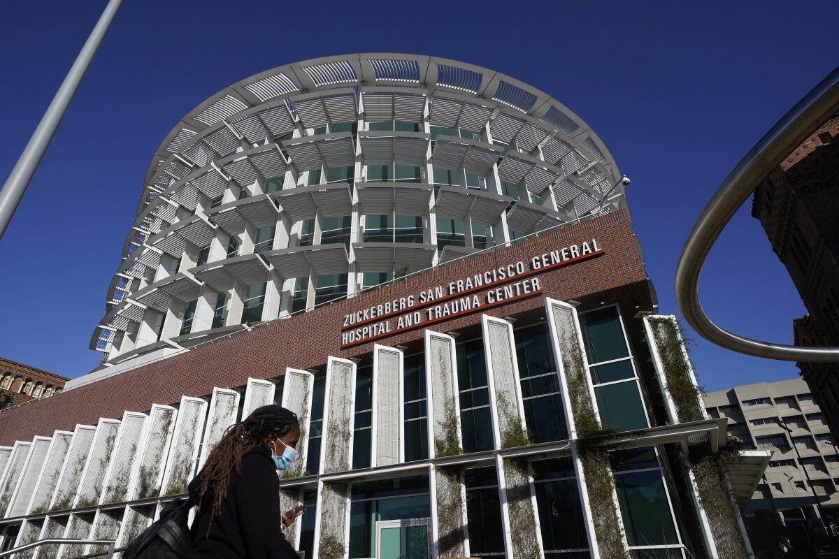 A woman wearing a mask walks under a sign for Zuckerberg San Francisco General Hospital and Trauma Center in San Francisco.