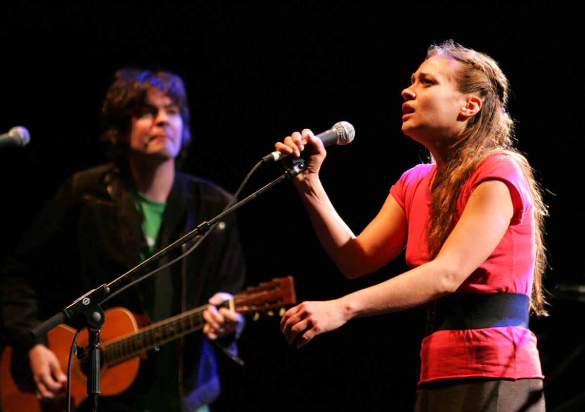 A male guitarist and female singer perform onstage