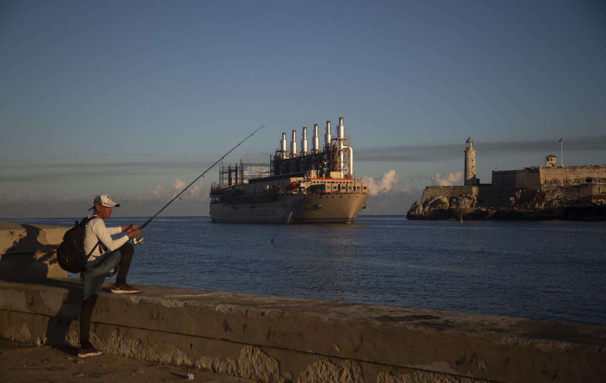 Un pescador sostiene su caña en el malecón, donde un barco de bandera turca llega a la bahía 