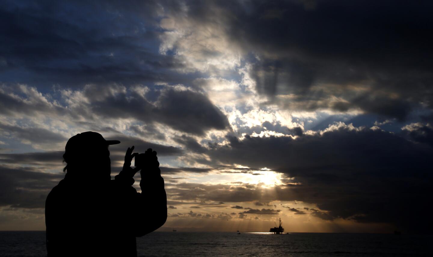 A man photographs the sun filtering through heavy clouds in Huntington Beach.