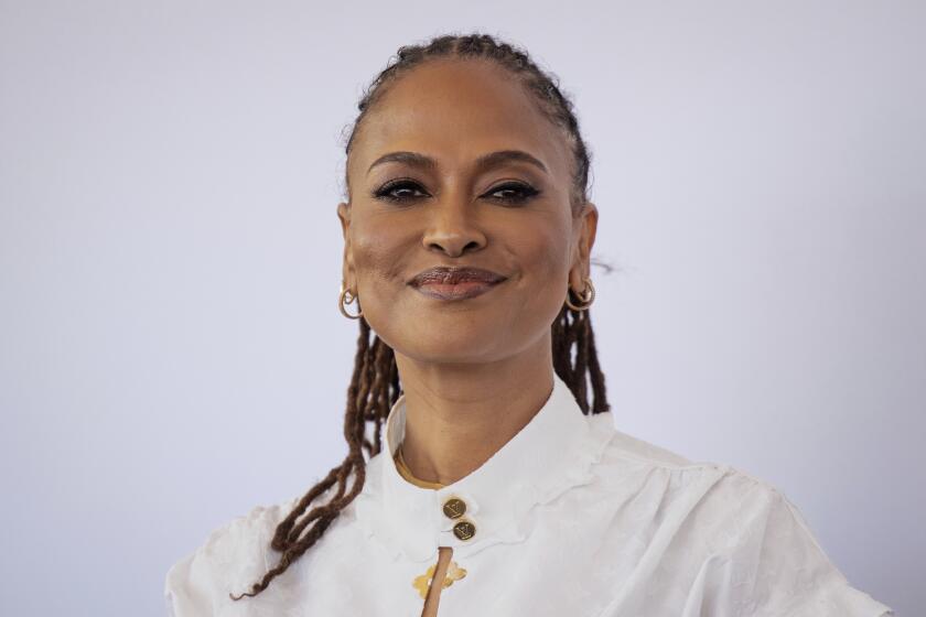 Ava DuVernay smiles in a collared white shirt against a white backdrop.