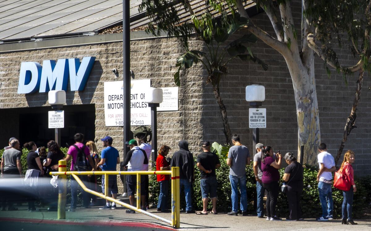 A line of people waiting outside a brick building with a sign that reads "DMV"