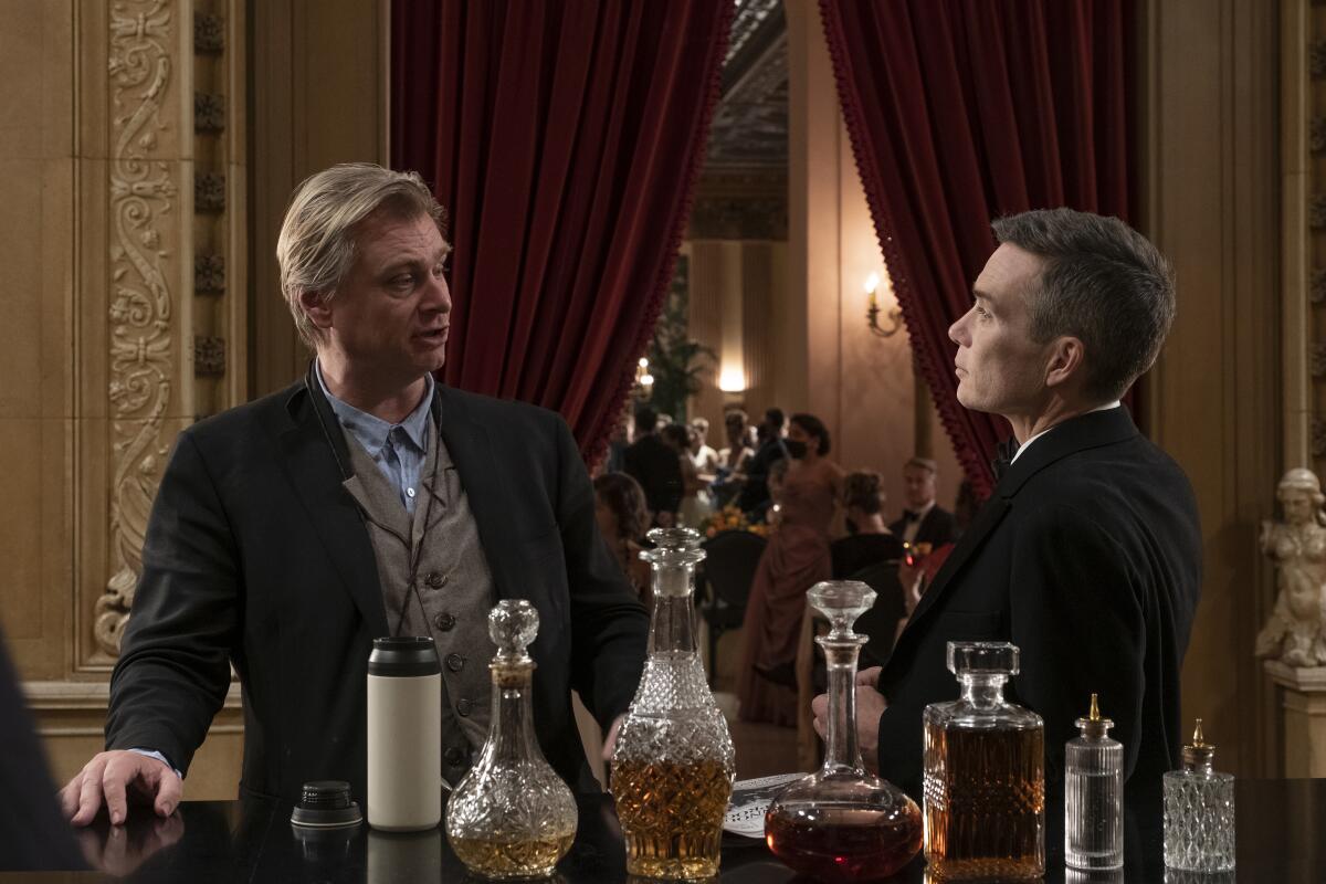 Nattily dressed director Christopher Nolan talks with Cillian Murphy (J. Robert Oppenheimer) on an opulent hotel set.