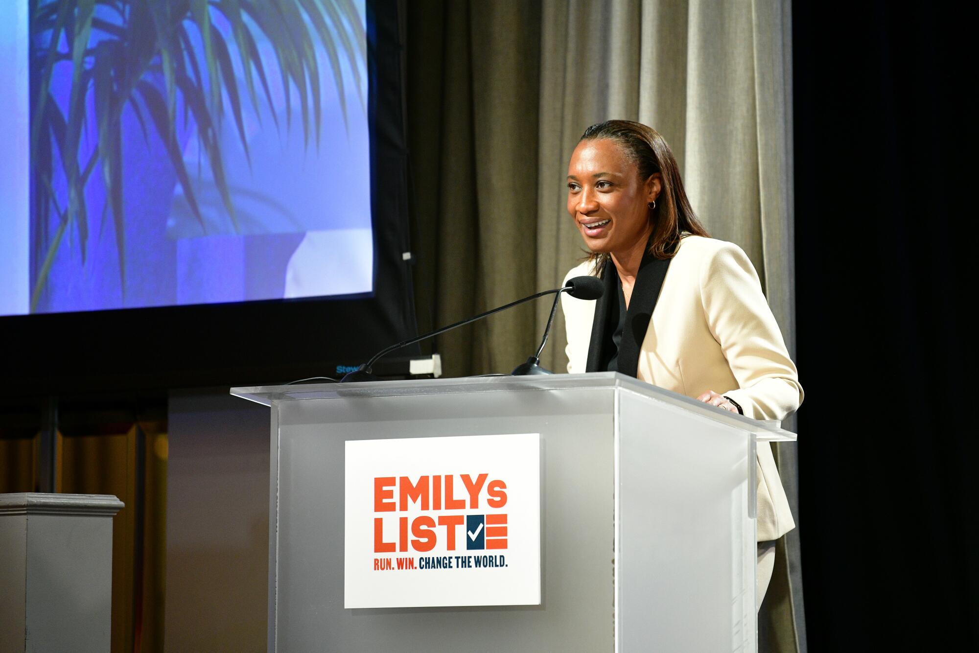 Laphonza Butler speaks at a lectern with an Emily's List sign on it 