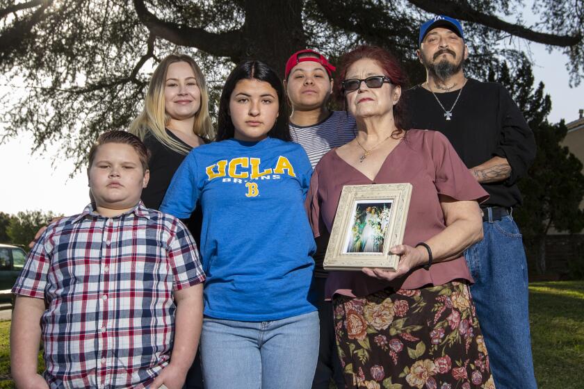 DOWNEY, CA -- FRIDAY, APRIL 3, 2020: Jennifer Soto, 17, third from left, shown with her family: Zack Pack, 11, Rose Pack, 21, Sara Bernard, 21, widow Chris Bernard, holding her 1988 wedding photo of her and husband Alex Bernard, 57, and Ismael Moreno at their Downey home. Soto is a lacrosse player from Downey High, was a four-year starter and a very good player, a 4.2 student, just got accepted to UCLA, and tragically lost her foster father, Alex Bernard, 57, to the coronavirus, COVID-19. Photo taken in Downey, CA, on April 3, 2020. (Allen J. Schaben / Los Angeles Times)