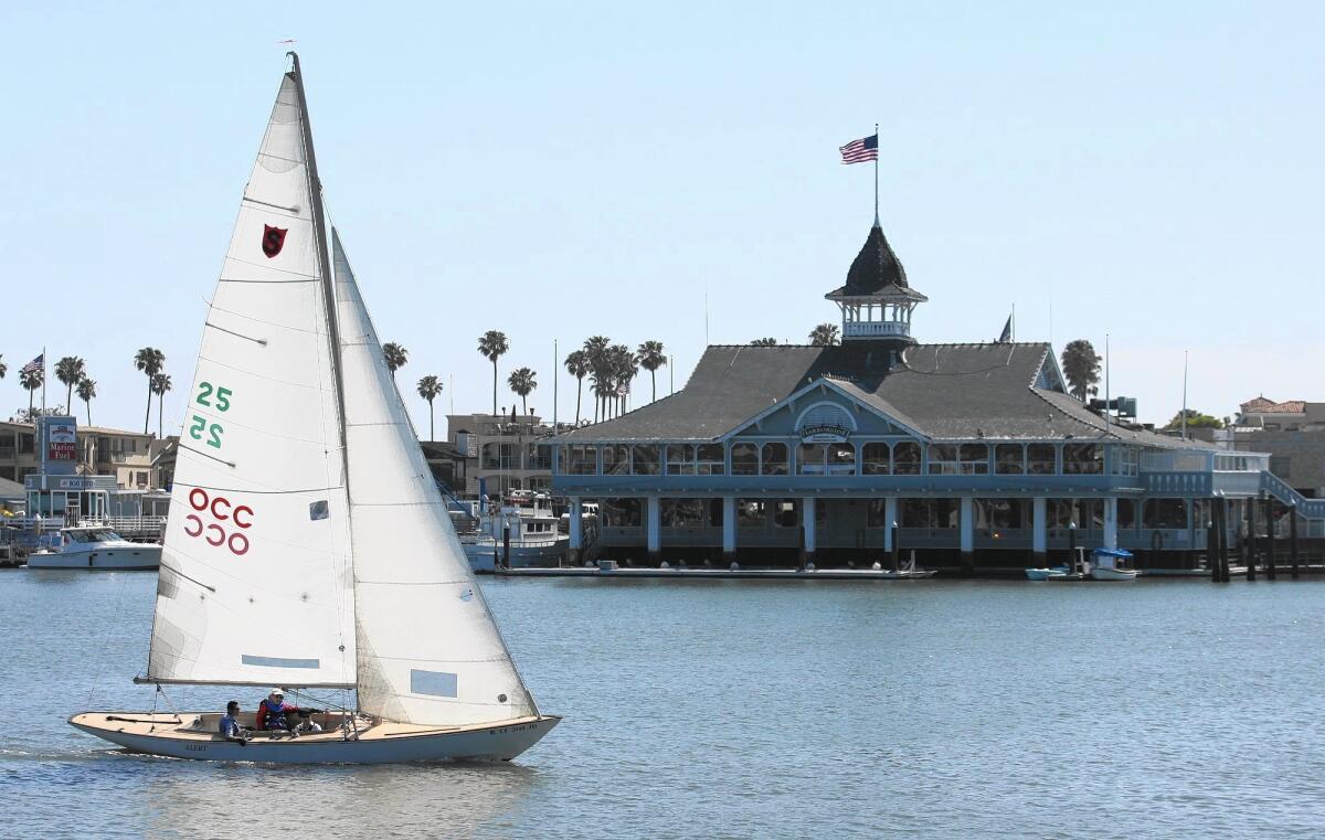 A sailboat glides past the Balboa Pavillion, built in 1905 by the Newport Bay Investment Co.