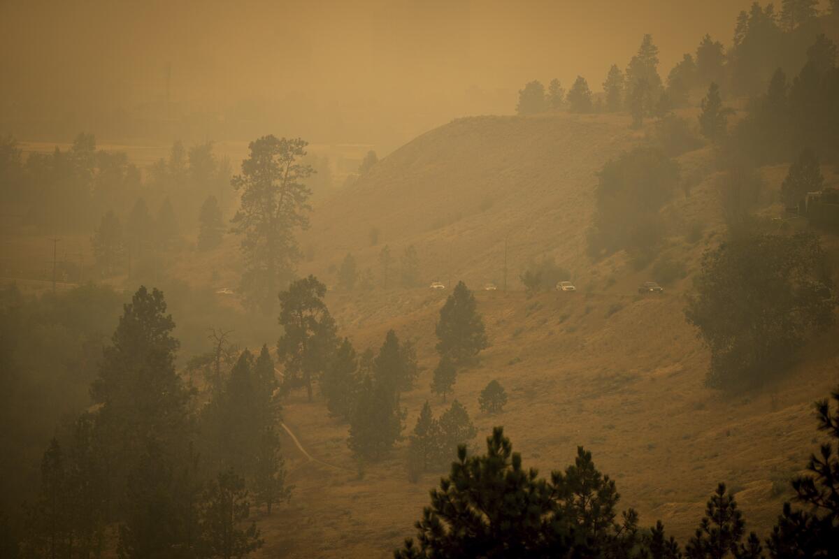 Smoke from wildfires fills the air as motorists travel on a road on the side of a mountain.