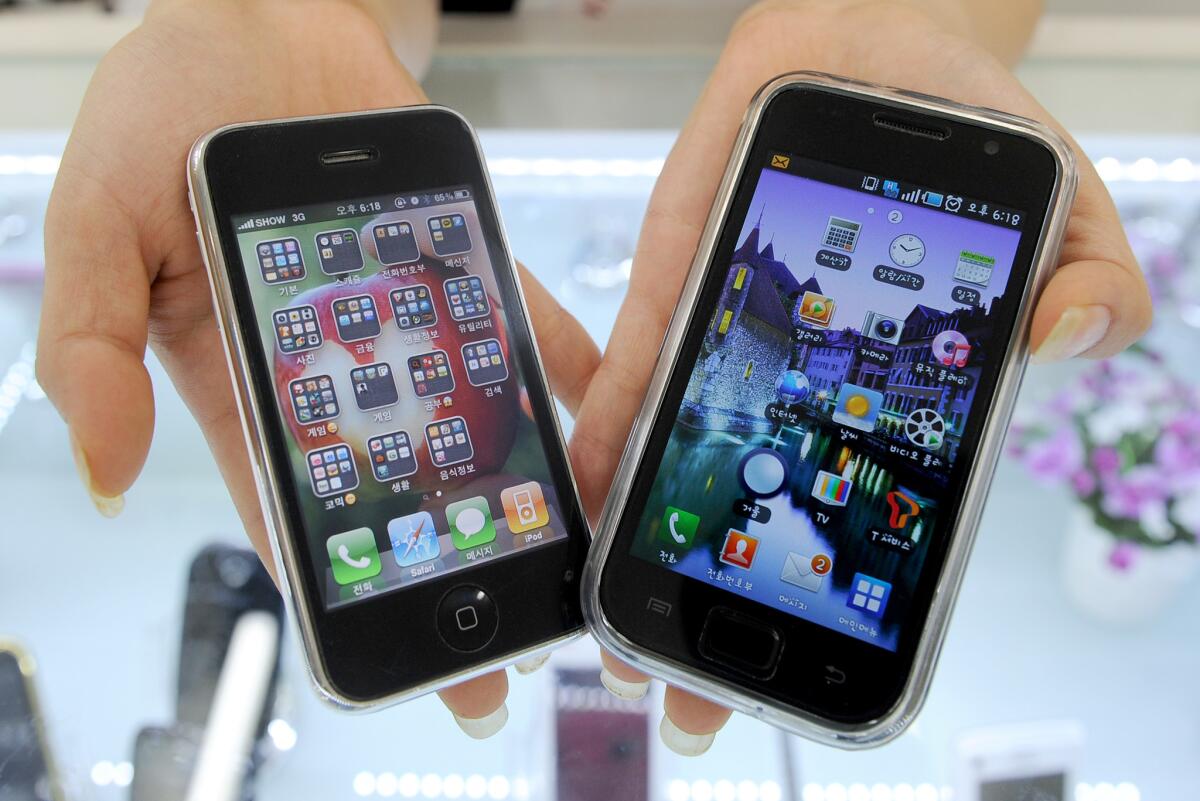 A shop manager shows Samsung's Galaxy S phone, right, and Apple's iPhone at a shop in Seoul.