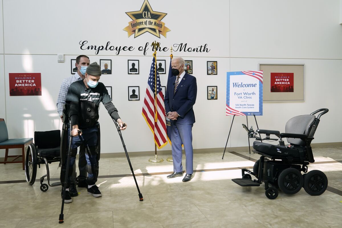 President Joe Biden watches as veteran John Caruso walks with the help of an exoskeleton and is assisted by Joshua Geering, SCI Therapy Lead Therapist, Spinal Cord Injury/Disabilities Center in Dallas, as Biden tour's the Fort Worth VA Clinic in Fort Worth, Texas, Tuesday, March 8, 2022. (AP Photo/Patrick Semansky)