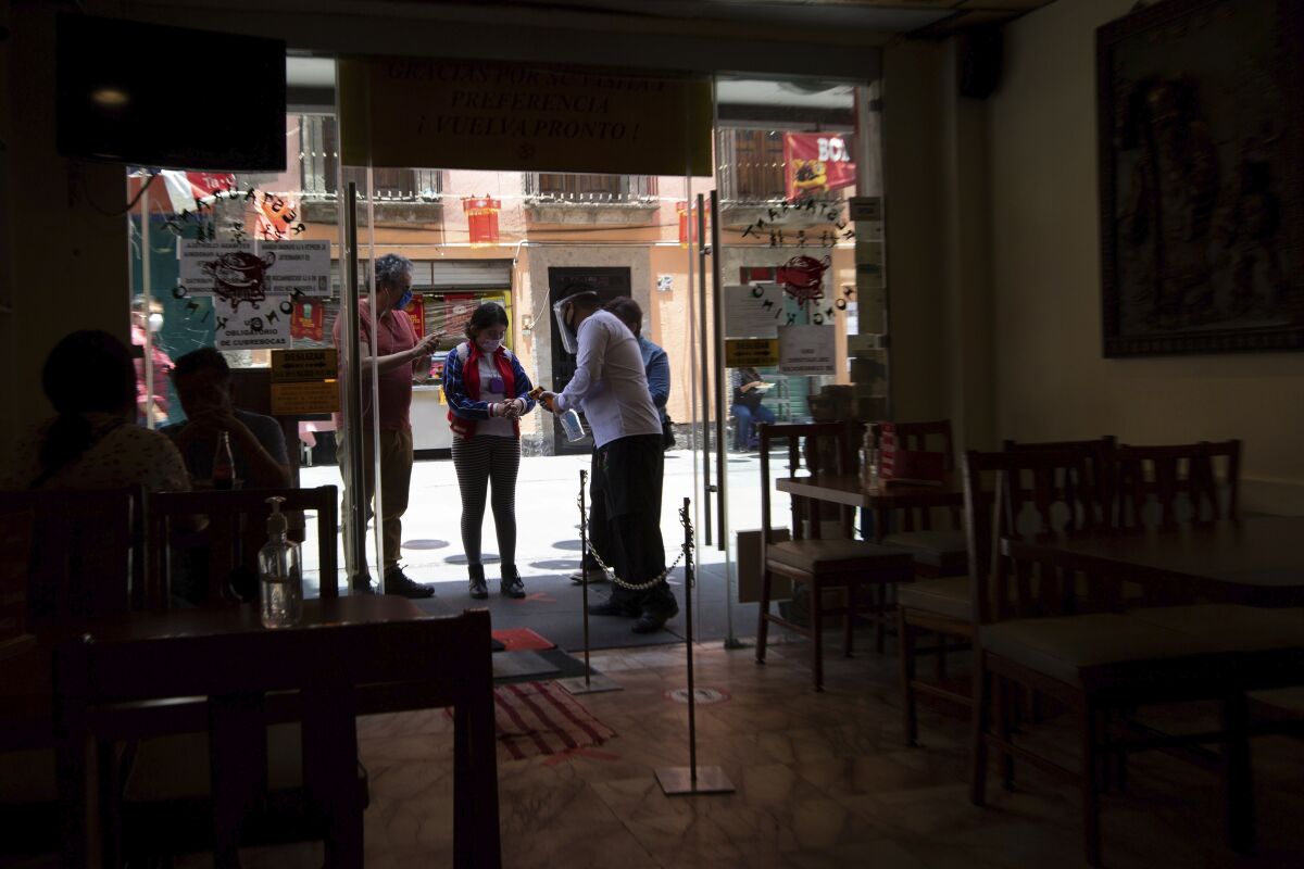 A waiter hands out disinfectant to customers before entering a Chinese restaurant in downtown Mexico City, Friday, July 3, 2020. Limited reopening of restaurants and other businesses in the capital this week came as new coronavirus cases continued to climb steadily. (AP Photo/Fernando Llano)