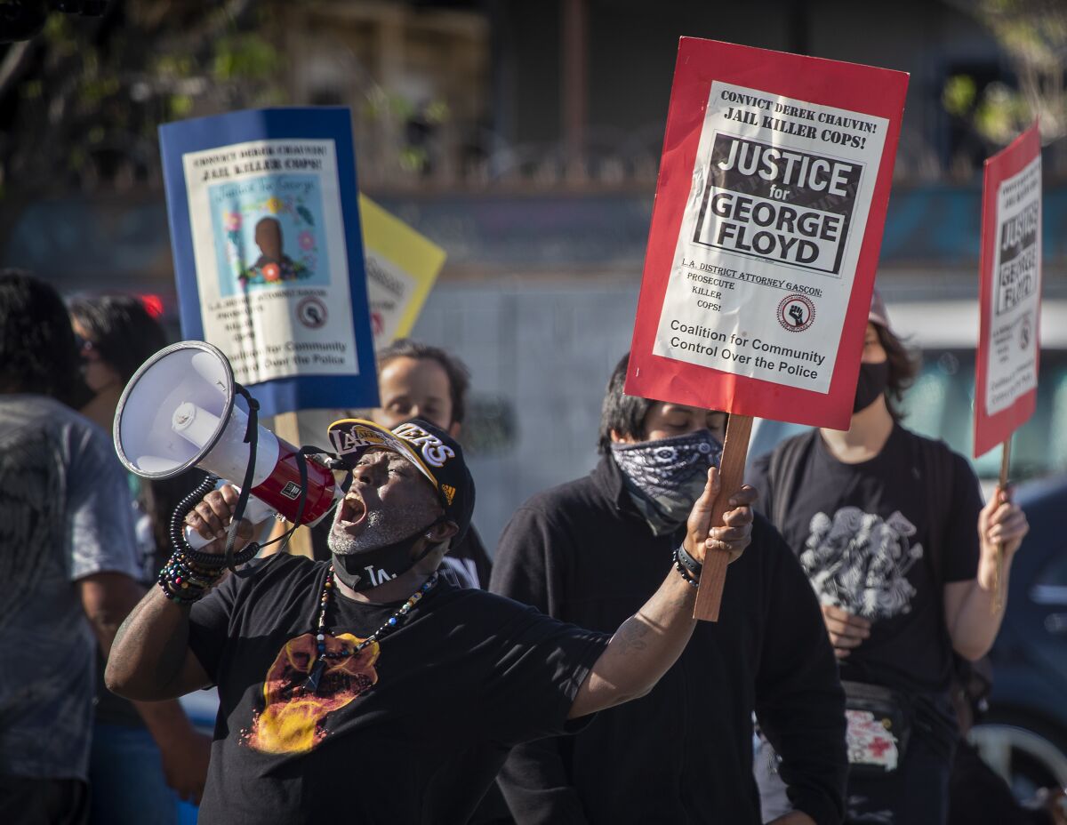 A man shouts into a megaphone and holds a "Justice for George Floyd" sign