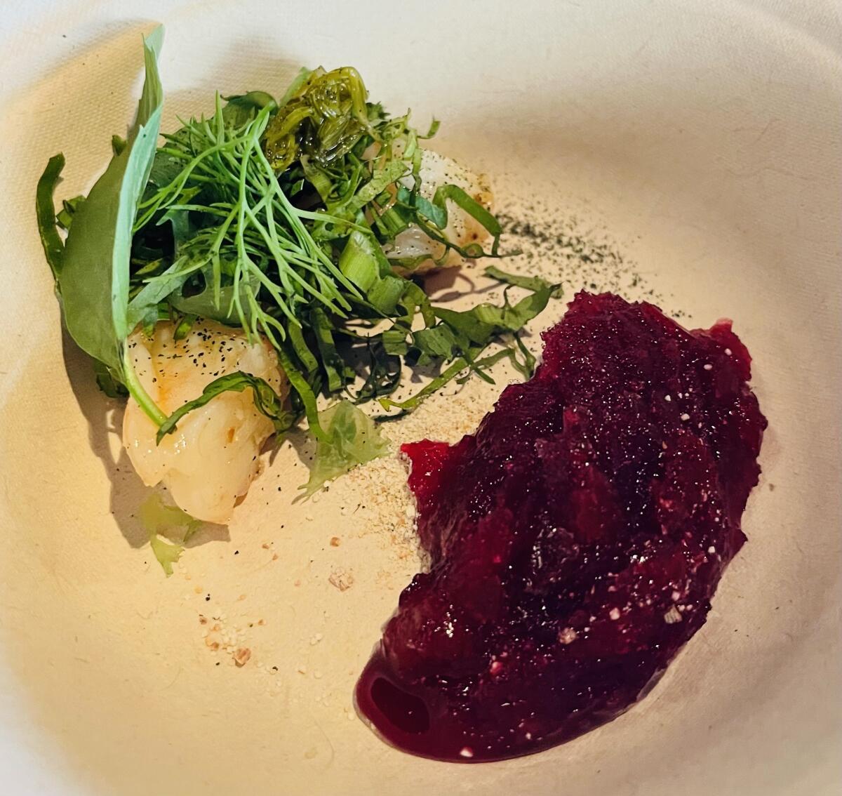 A plate holds a prawn, greens and a red sorbet.