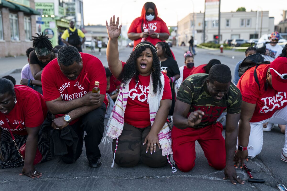 A group of mourners kneel on the ground and pray.