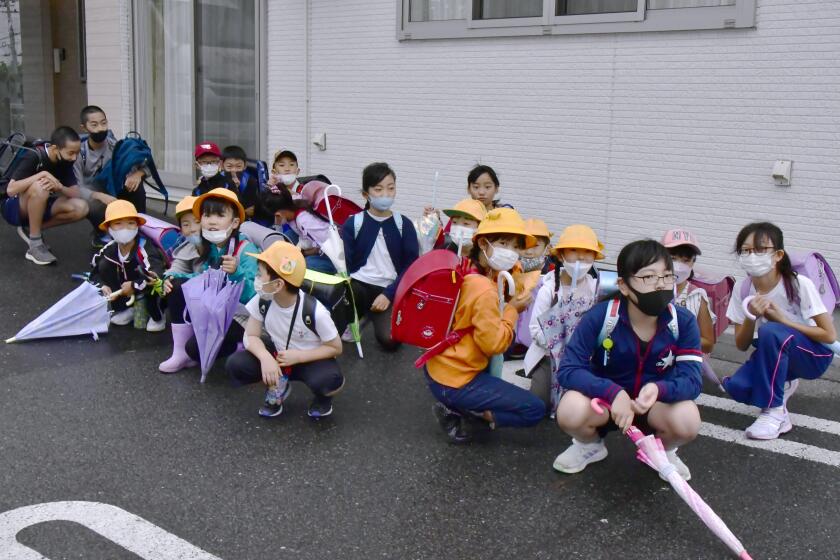 Elementary school students find shelter near a building on their way to school soon after a report of North Korea's missile launch, in Misawa, Aomori prefecture, northern Japan Tuesday, Oct. 4, 2022. North Korea on Tuesday fired an intermediate-range ballistic missile over Japan for the first time in five years, forcing Japan to issue evacuation notices and suspend trains during the flight of the weapon that is capable of reaching the U.S. territory of Guam. (Toonippo/Kyodo News via AP)