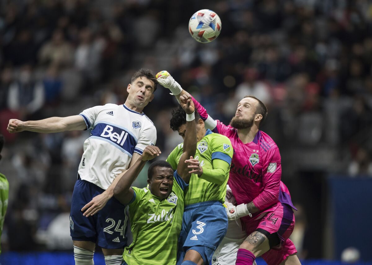 Seattle Sounders goalkeeper Stefan Frei, right, punches the ball away from Vancouver Whitecaps' Brian White, left, as Sounders' Nouhou Tolo, second from left, and Xavier Arreaga (3) defend during the first half of an MLS soccer match in Vancouver, British Columbia, Sunday, Nov. 7, 2021. (Darryl Dyck/The Canadian Press via AP)