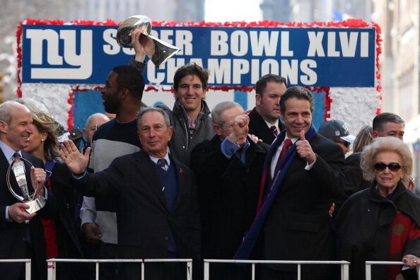 Eli Manning, quarterback of the New York Giants holds the Vince Lombardi Trophy next to (L-R) Justin Tuck, defensive end of the New York Giants; Mayor of New York City Michael Bloomberg; Tom Coughlin, head coach of the New York Giants; and Governor of New York Andrew Cuomo during The New York Giants' Victory Parade along the Canyon of Heroes in downtown New York on February 7, 2012 in New York City.