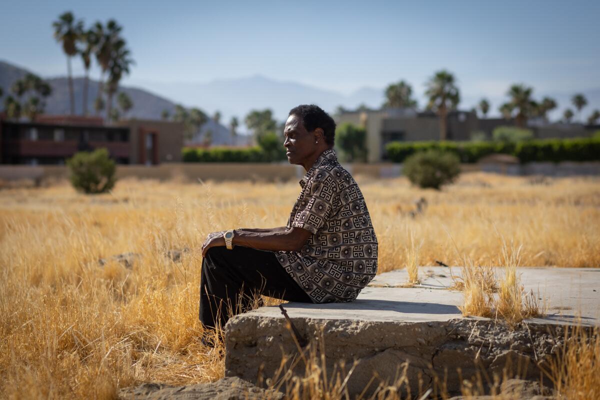 A man sits on a slab of concrete in a desert lot.