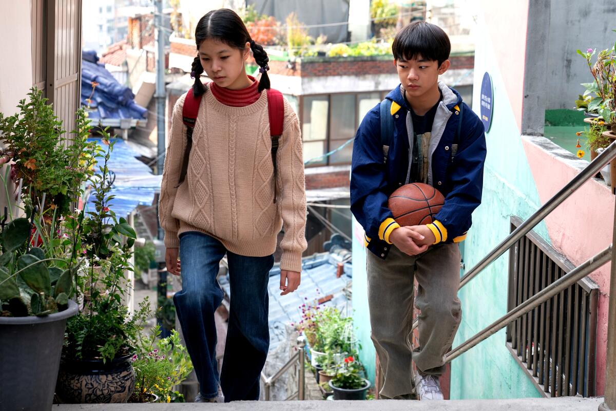 A girl and a boy, he carrying a basketball, walk up an outdoor staircase.