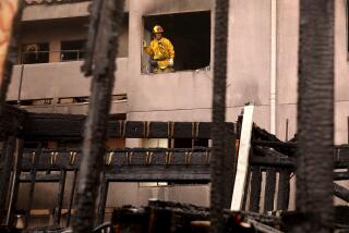 LOS ANGELES, CA - SEPTEMBER 13, 2024 - A firefighter looks out from a fire damaged apartment over the remnants of a three story building that was under construction, foreground, at 800 N. Bunker Hill Ave. in Chinatown on September 13, 2024. The fire started at a vacant three-story apartment building, under construction, and spread to nearby apartment buildings. Around 30 apartment tenants are displaced by the fire. According to L.A.F.D. Captain and Pio Adam VanGerpen, one person is in critical condition after being rescued from the raging fire and two firefighters suffered injuries. 130 firefighters battled the blaze which started at 3:34 a.m. (Genaro Molina/Los Angeles Times)