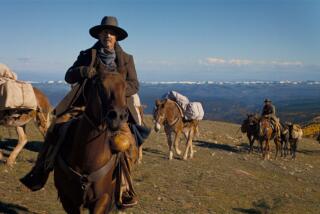 A man rides a horse on a mountain range, followed by pack horses.