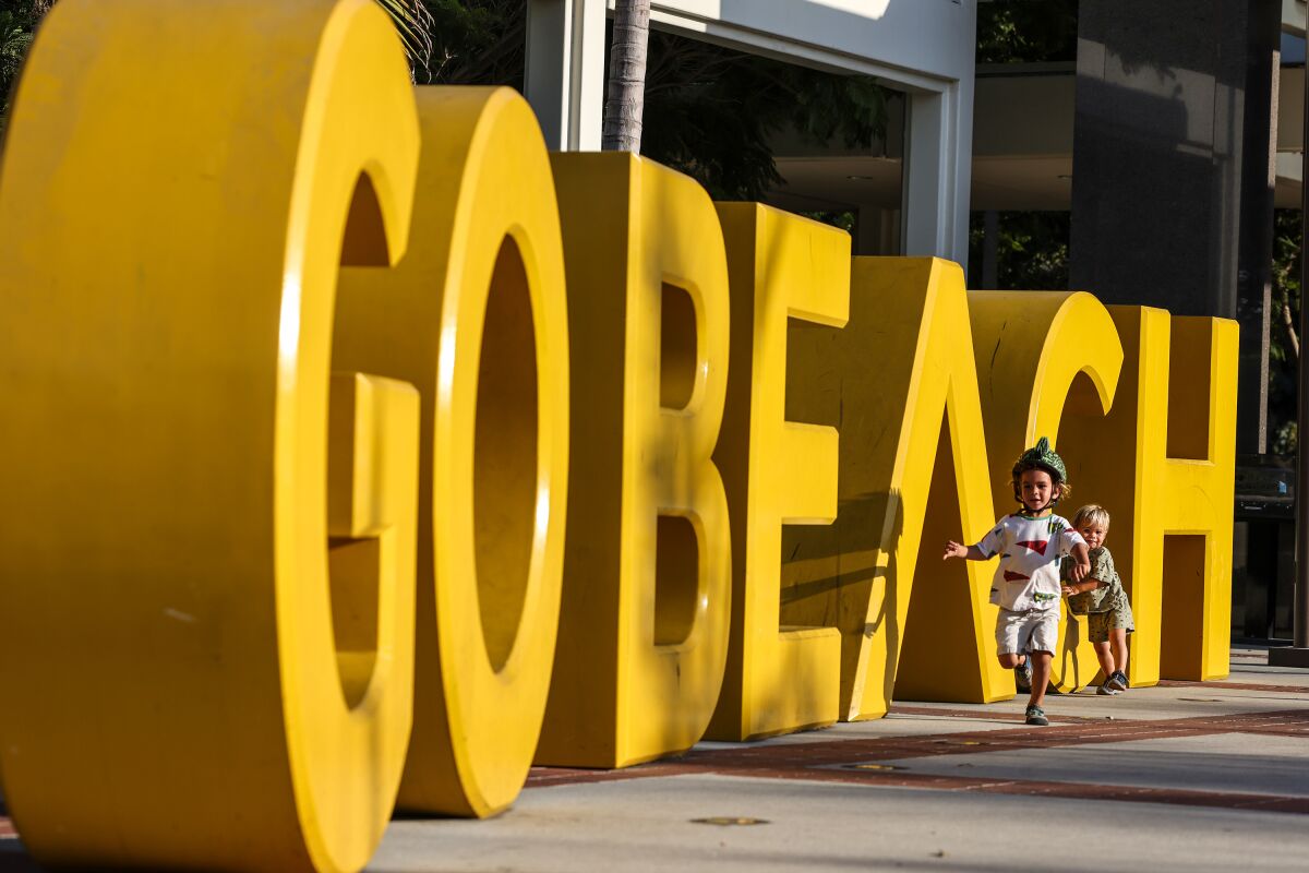 Two toddlers run next to giant yellow "GO BEACH" letters