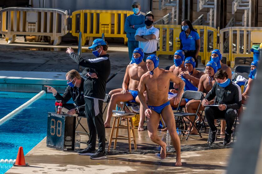UCLA men's water polo coach Adam Wright, left in hat, directs his players during a match.