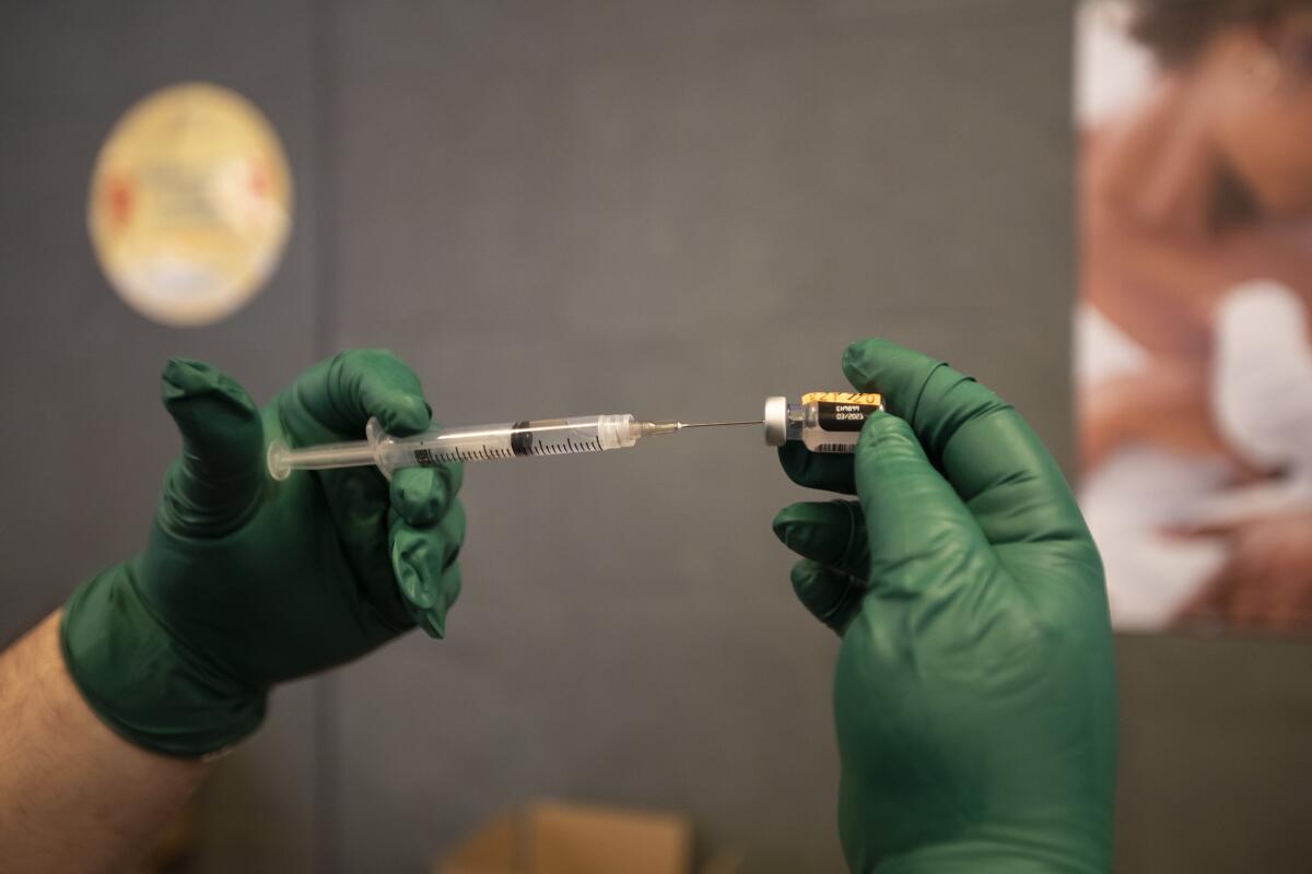 Gloved hands insert a syringe into a COVID-19 vaccine bottle
