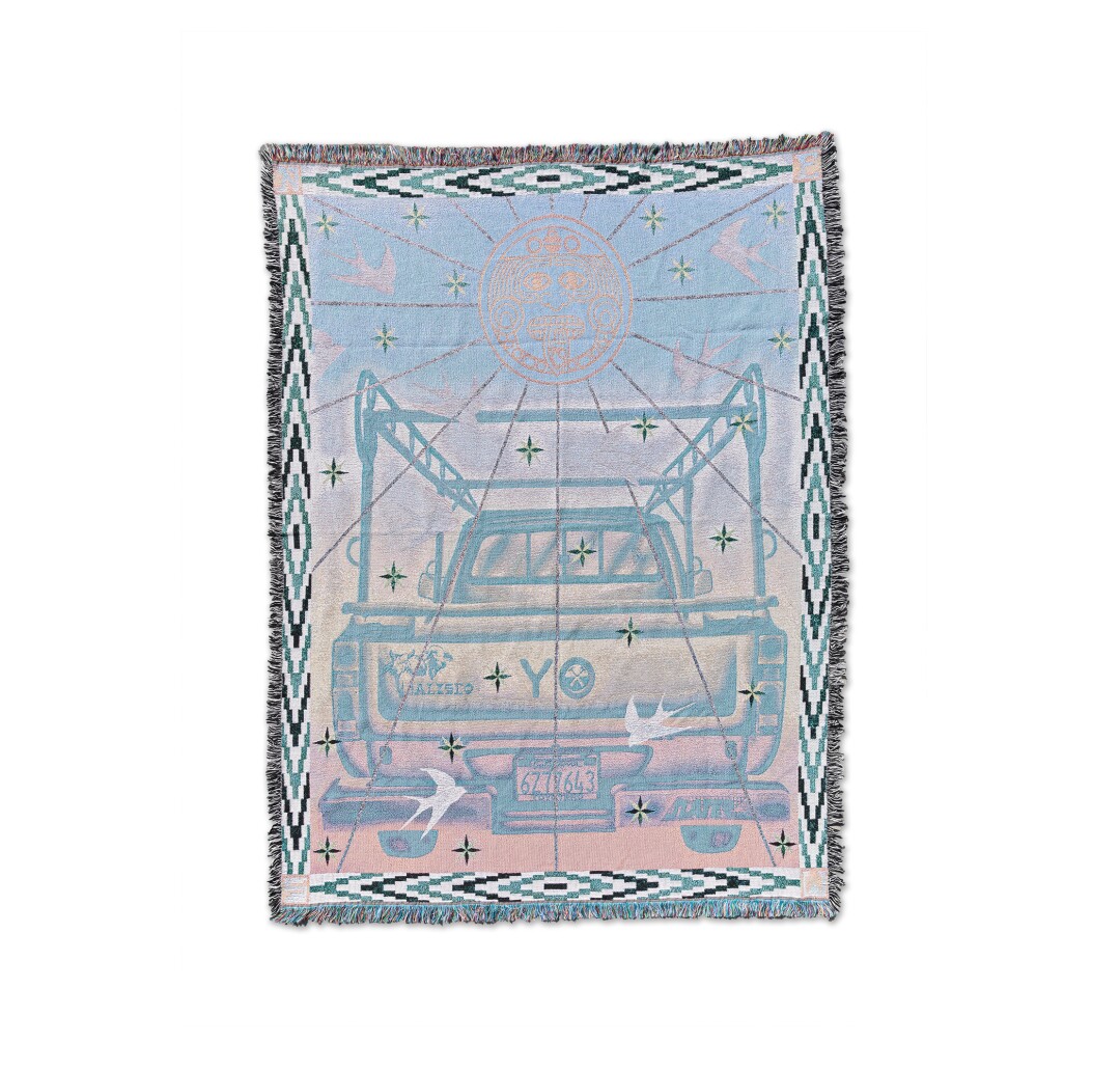 A blanket features a painting of a Toyota truck in cool shades of pink and blue and framed by geometric patterns.