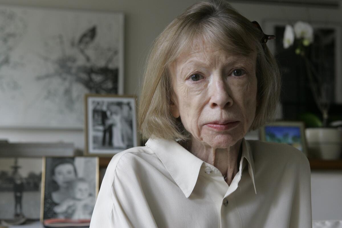 Joan Didion standing in an apartment in front of framed family photos