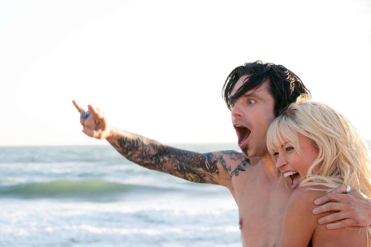A tattooed man and a blond woman celebrating on a beach