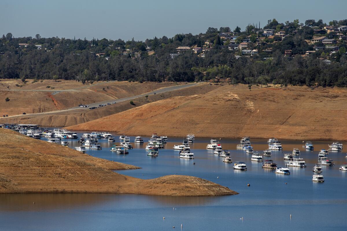 Boats are crowded into a small area of open water at Lake Oroville, surrounded by bare banks that were once submerged.