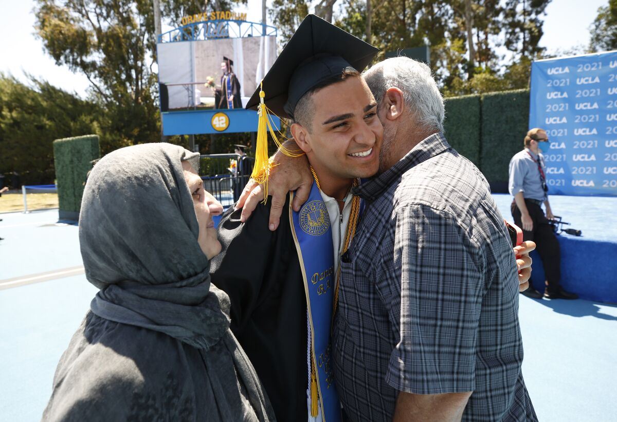 A smiling man in a graduation cap and gown hugs his mother and father.