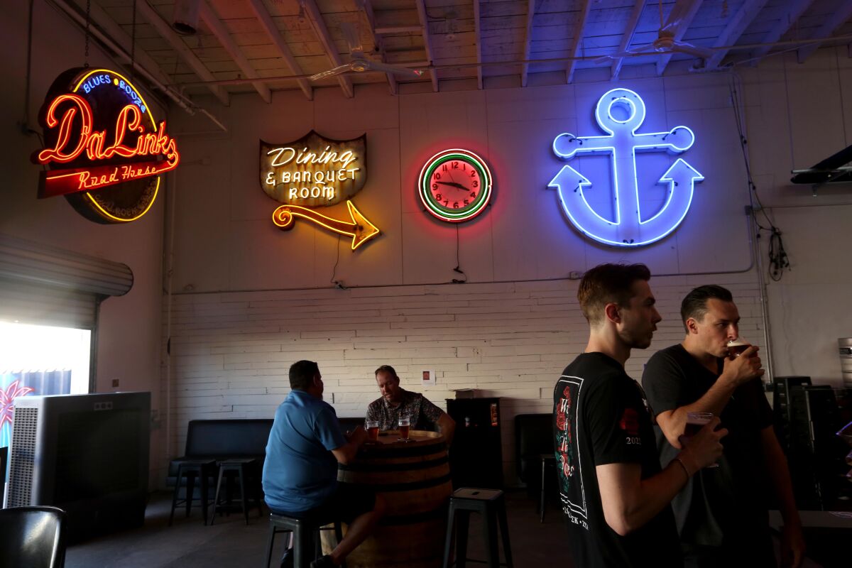 people sit inside a brewery with four neon signs above them