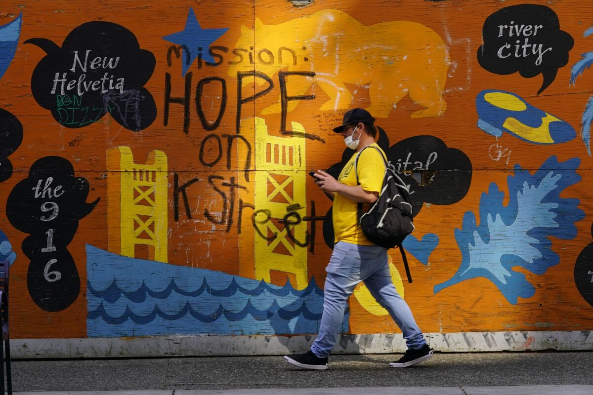 A man passes a colorful panel painted with the message "Mission: Hope on K Street," in Sacramento, Calif., Thursday, April 7, 2022. A mass shooting, April 3 that killed six people and wounded a dozen others occurred just a two blocks from where this sign is displayed. In recent years the heart of the city has been rattled by rising crime, protests and the economic drubbing of the pandemic. (AP Photo/Rich Pedroncelli)