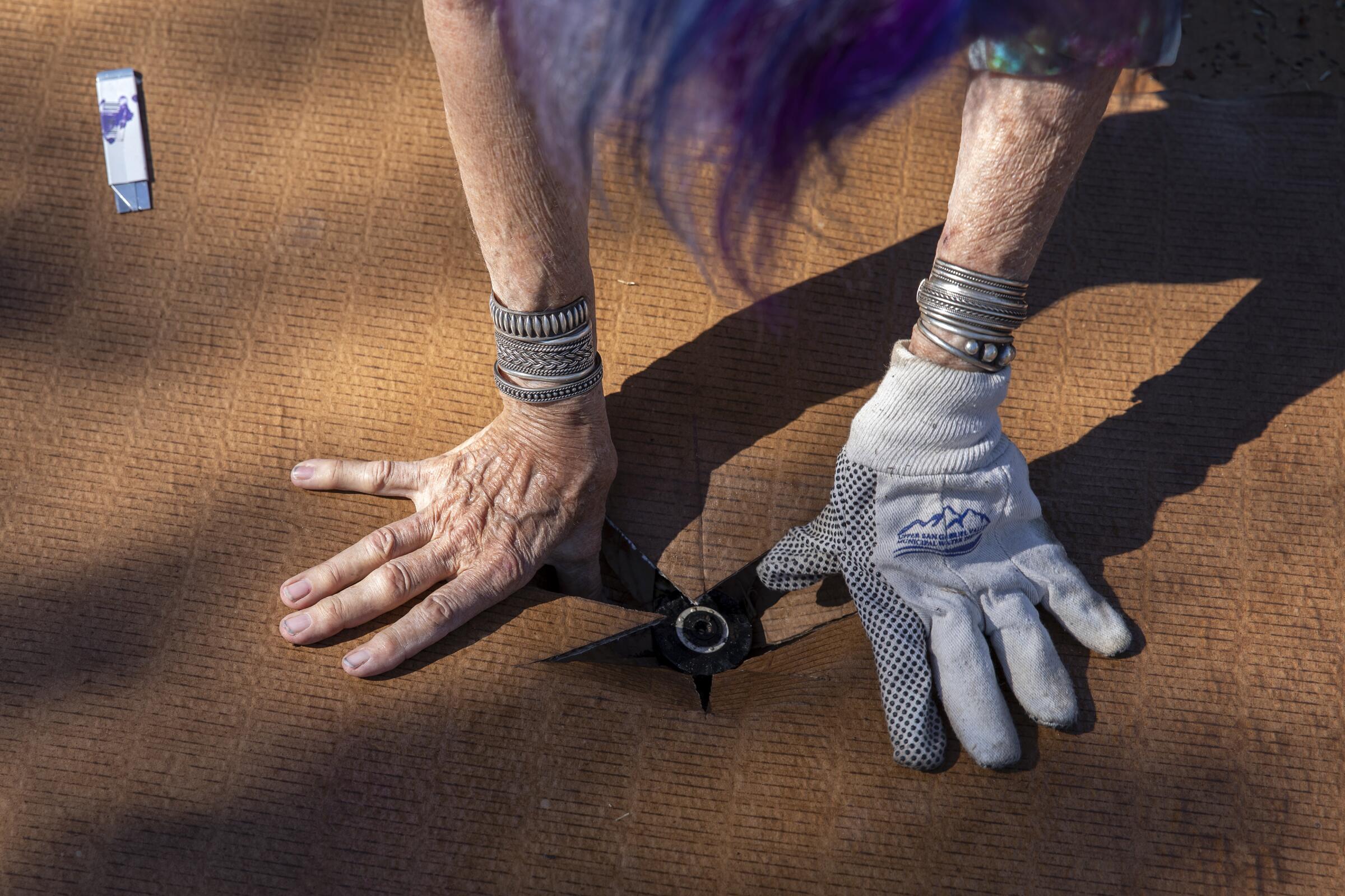 Two hands, one gloved, push open a hole in cardboard around a sprinkler head. 