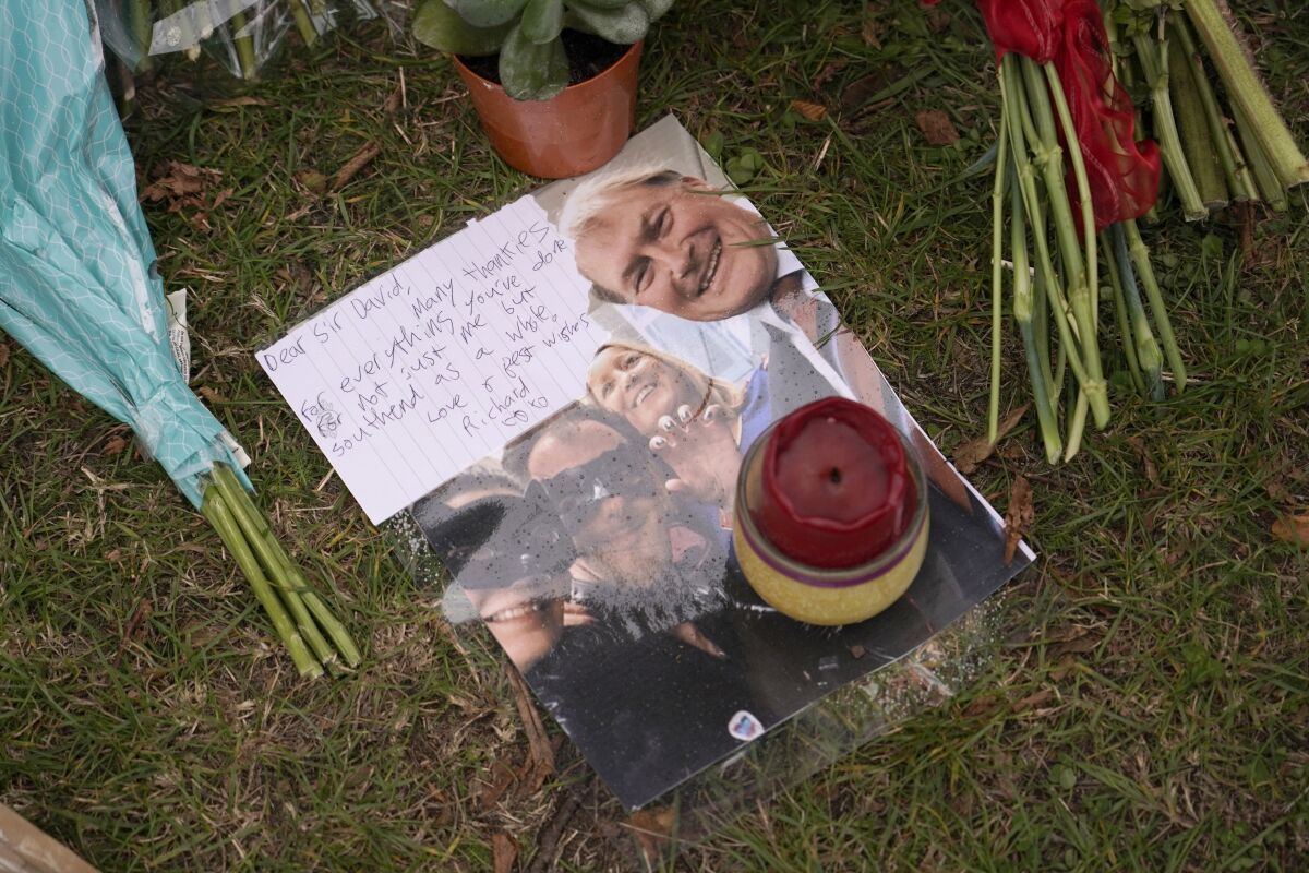A note is seen on a photograph showing slain member of Parliament David Amess, right, placed by a floral tribute near the scene where Amess was killed on Friday, in Leigh-on-Sea, Essex, England, Saturday, Oct. 16, 2021. Amess, a long-serving member of Parliament was stabbed to death during a meeting with constituents at a church in Leigh-on-Sea on Friday, in what police said was a terrorist incident. A 25-year-old British man is in custody. (AP Photo/Alberto Pezzali)