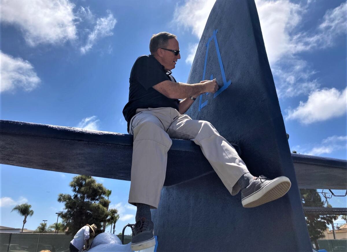 Costa Mesa police Capt. Vic Bakkila makes an "A" stencil on a fighter jet at Lions Park in Costa Mesa on Friday.