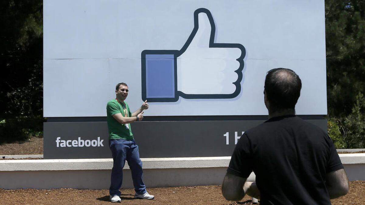 A man poses for photographs in front of the Facebook sign on the company's campus in Menlo Park, Calif.